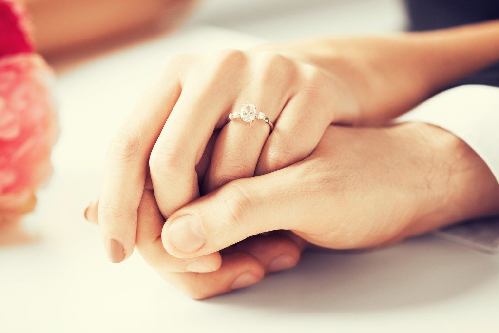 Female wearing engagement ring while hand being held by man
