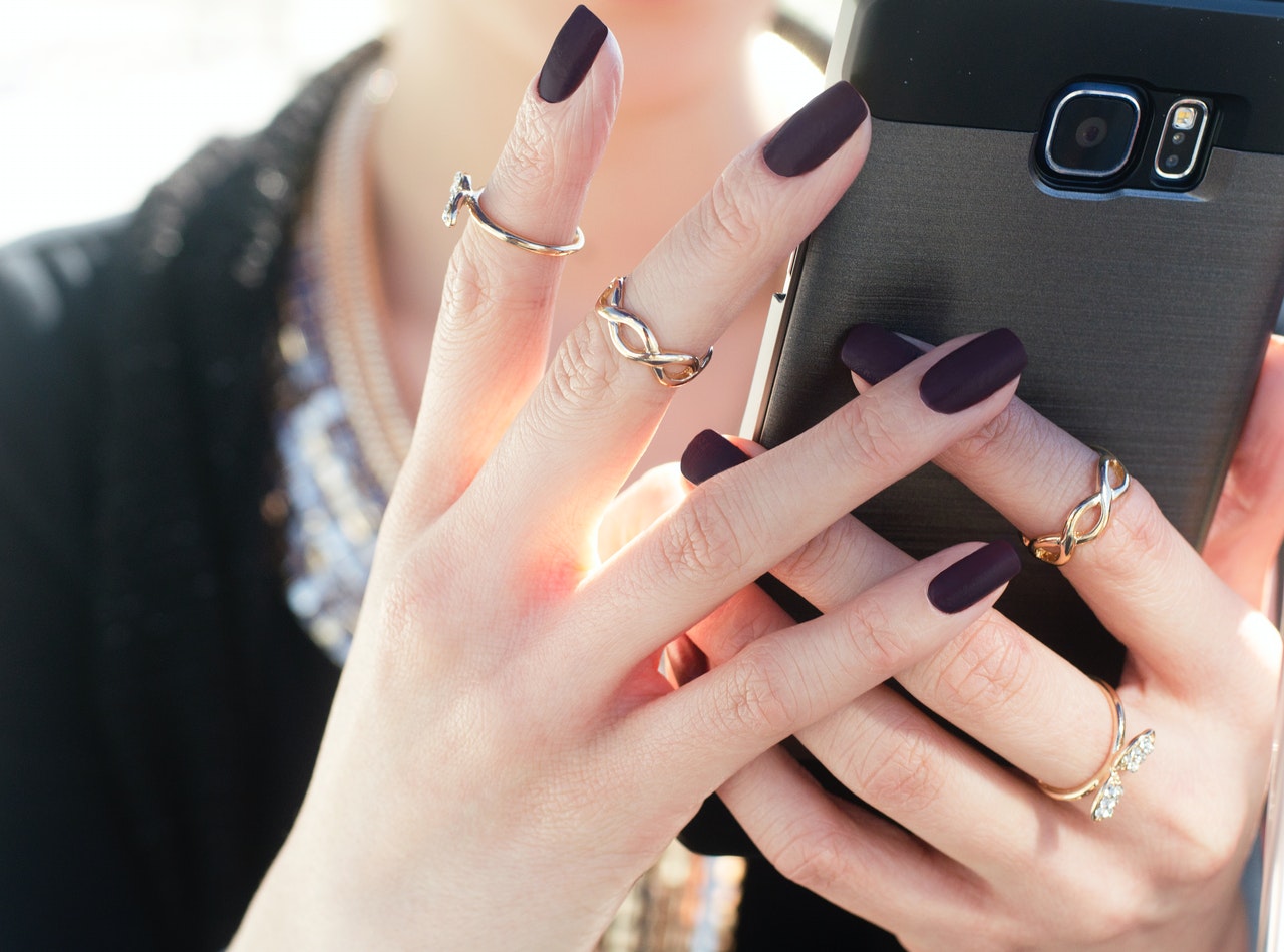 woman with nail polish holding smart phone