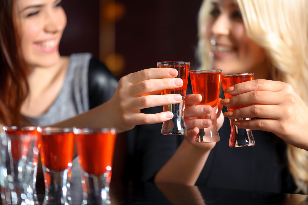 Selective focus on three shots with red beverage and smiling girls in blurry holding glasses