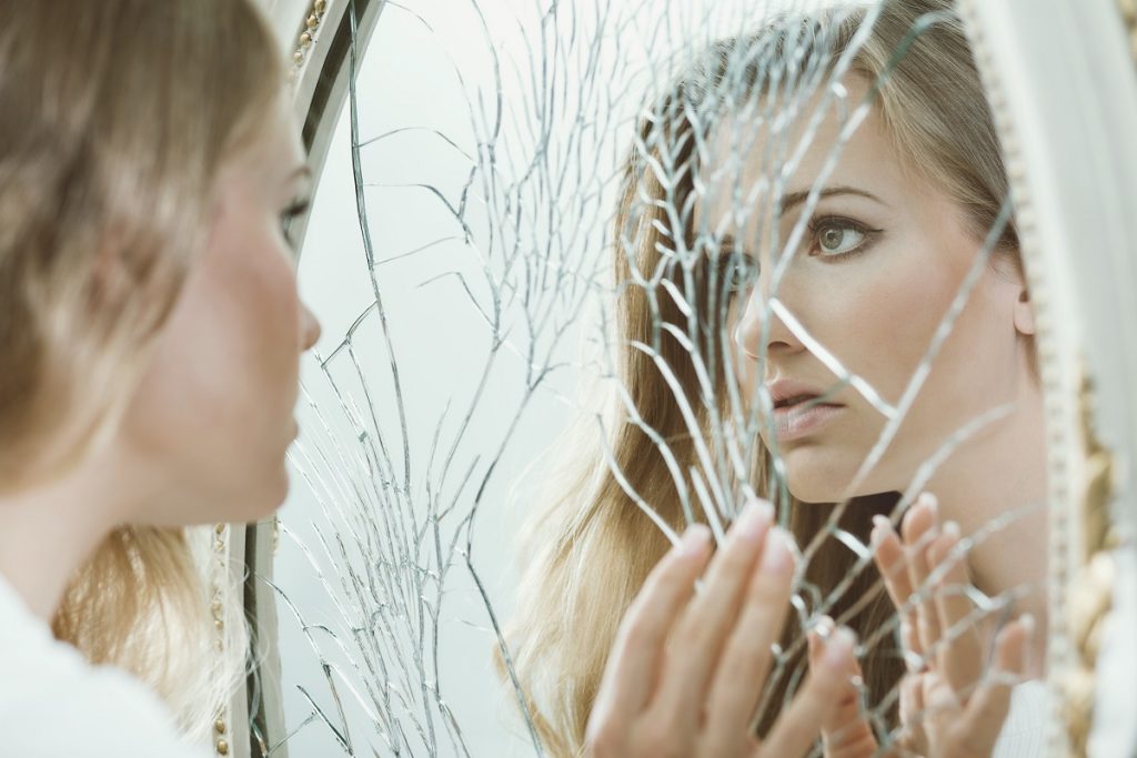 a teenager looking in the broken mirror