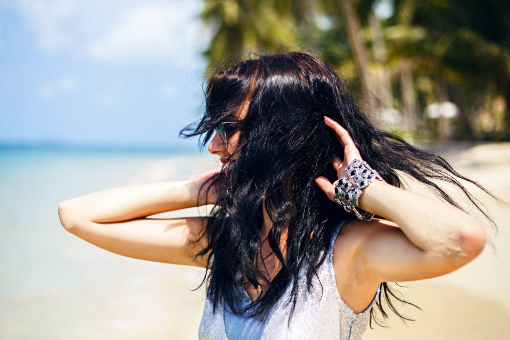 woman on the beach playfully flipping her long, black hair