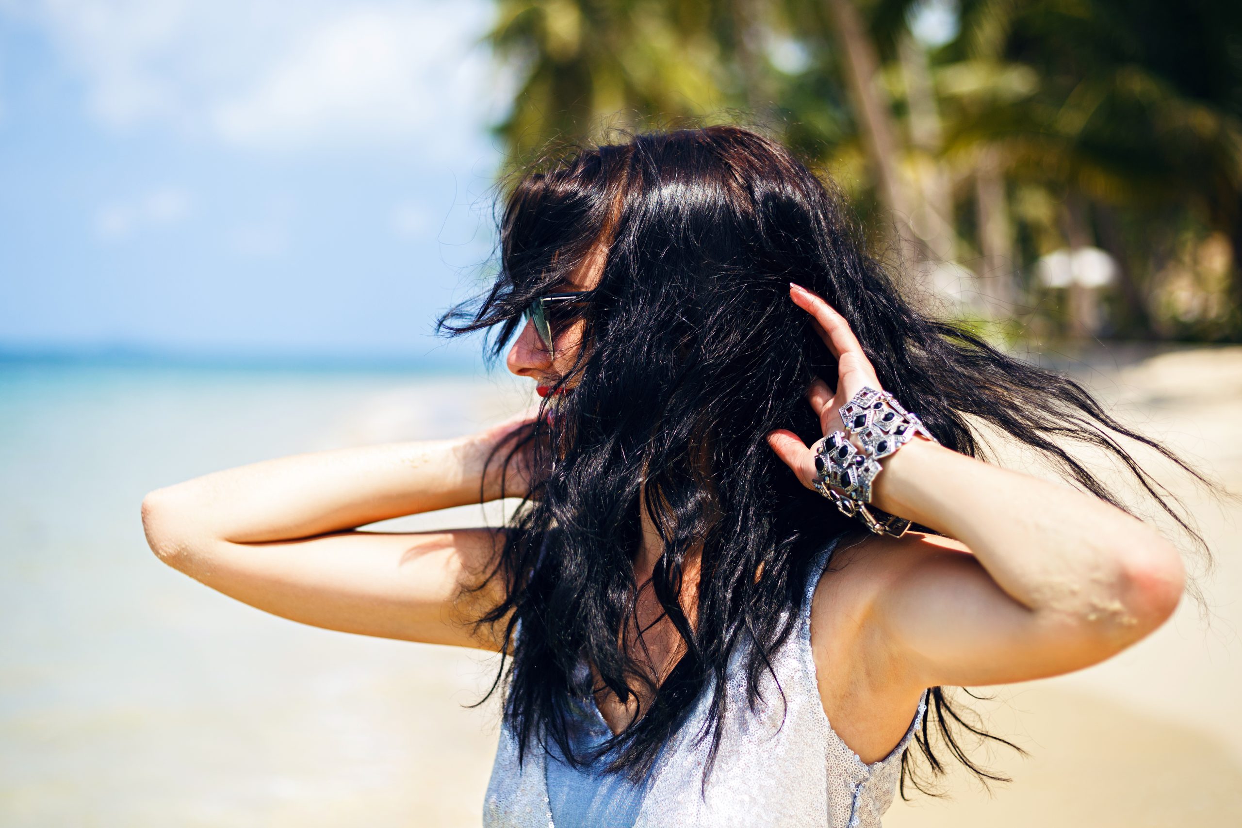 woman on the beach playfully flipping her long, black hair