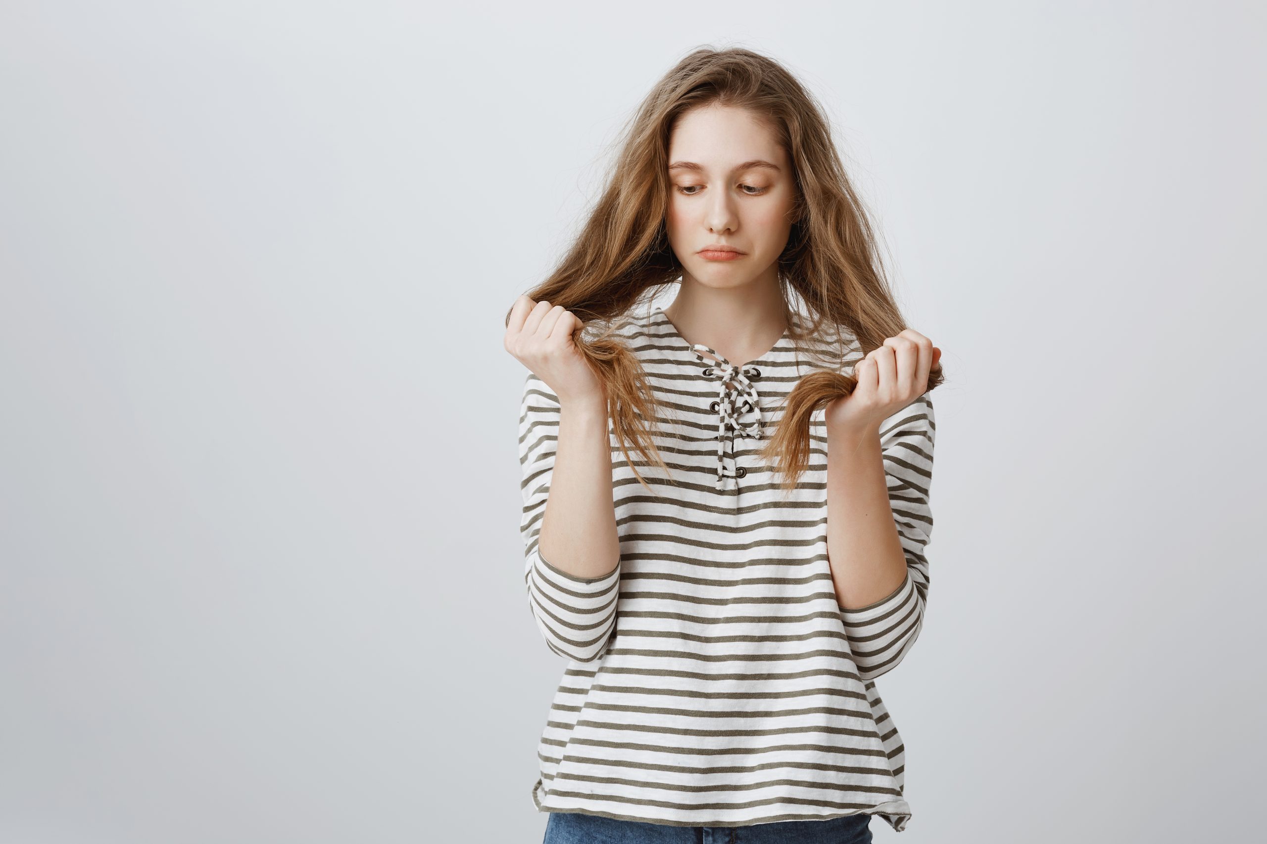 gloomy woman holding the ends of her hair and looking at them