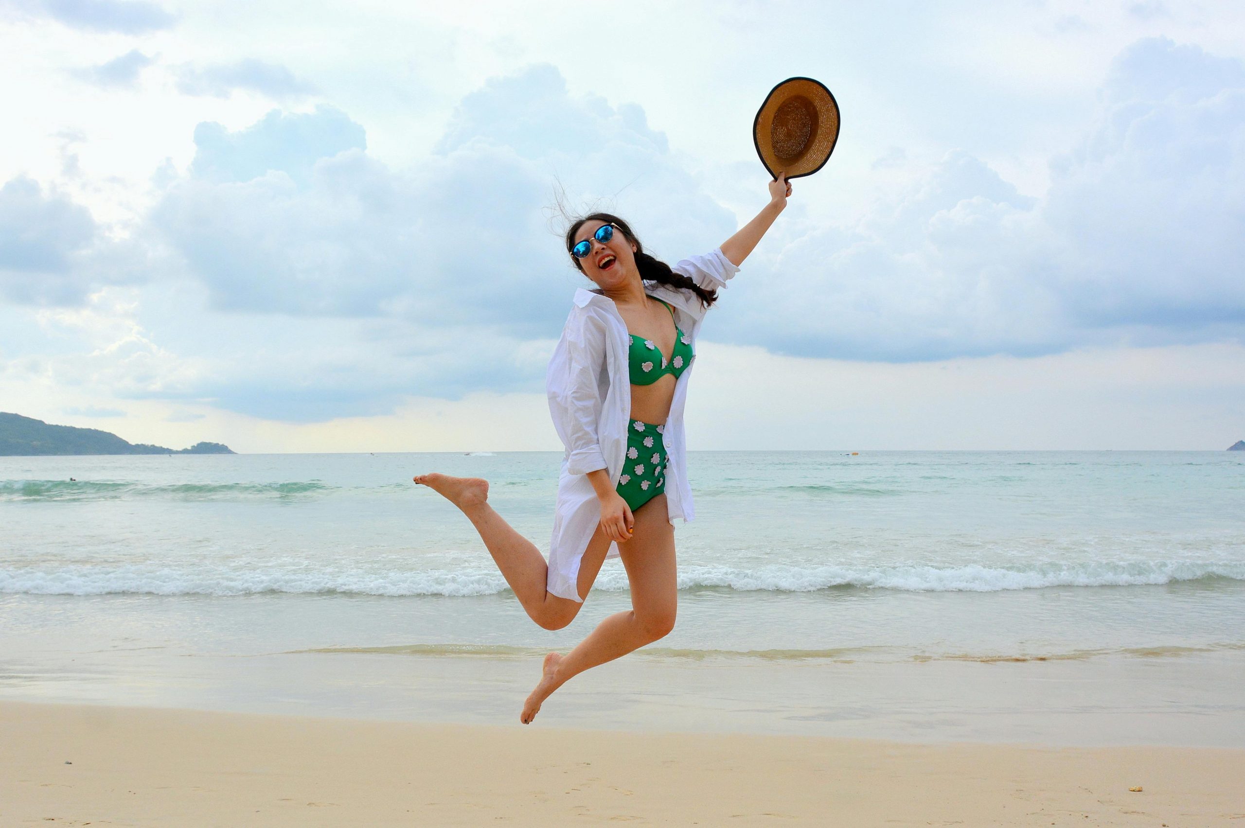 smiling woman with braided hair jumping on the beach mid-air